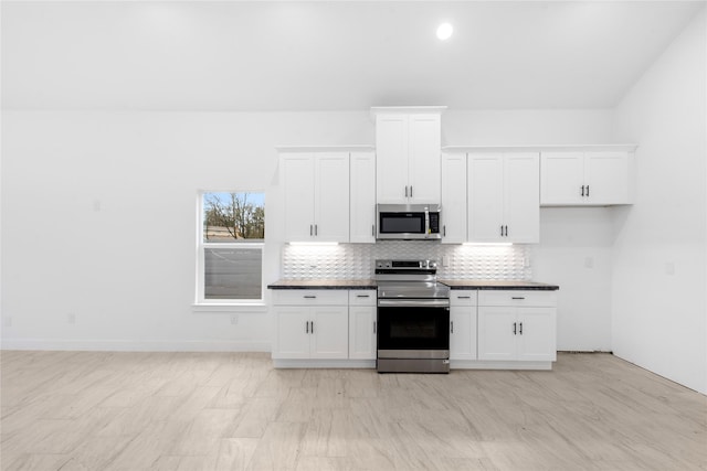 kitchen featuring tasteful backsplash, white cabinets, dark countertops, stainless steel appliances, and baseboards