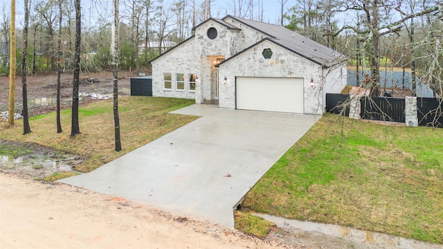 view of front of house featuring fence, stone siding, a front lawn, a garage, and driveway