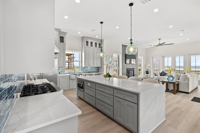 11370 Beachside, Galveston, TX 77554 - kitchen with light wood-style flooring, a ceiling fan, gray cabinets, a center island, and backsplash