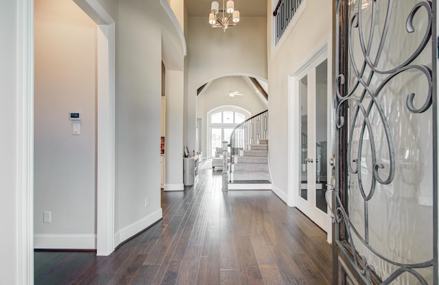entrance foyer with baseboards, arched walkways, a high ceiling, an inviting chandelier, and dark wood-style floors