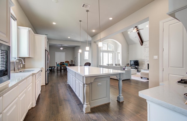 kitchen with open floor plan, a ceiling fan, a kitchen island, visible vents, and a sink