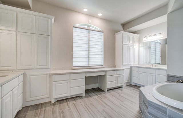 bathroom featuring two vanities, a healthy amount of sunlight, and a garden tub