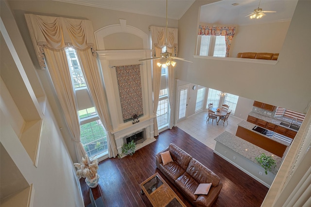living room featuring a wealth of natural light, a towering ceiling, a ceiling fan, and crown molding