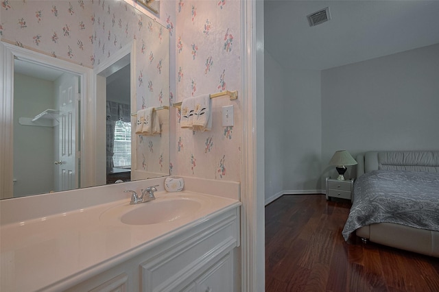 bathroom featuring vanity, baseboards, wallpapered walls, visible vents, and wood finished floors