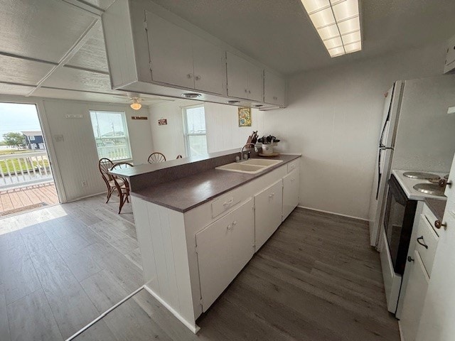 kitchen featuring a peninsula, light wood-style floors, white cabinets, a sink, and white electric stove