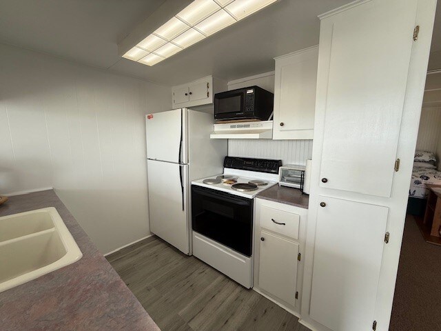 kitchen featuring white appliances, white cabinetry, a sink, and wood finished floors