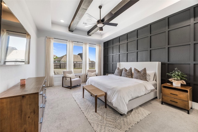 bedroom with visible vents, a raised ceiling, a decorative wall, ceiling fan, and light colored carpet