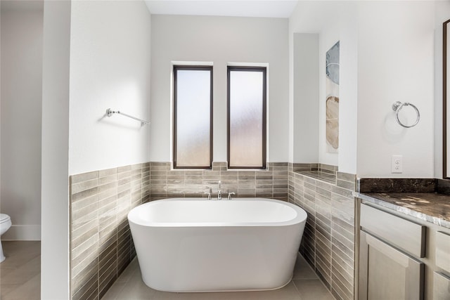 full bathroom featuring a freestanding tub, toilet, tile walls, vanity, and wainscoting