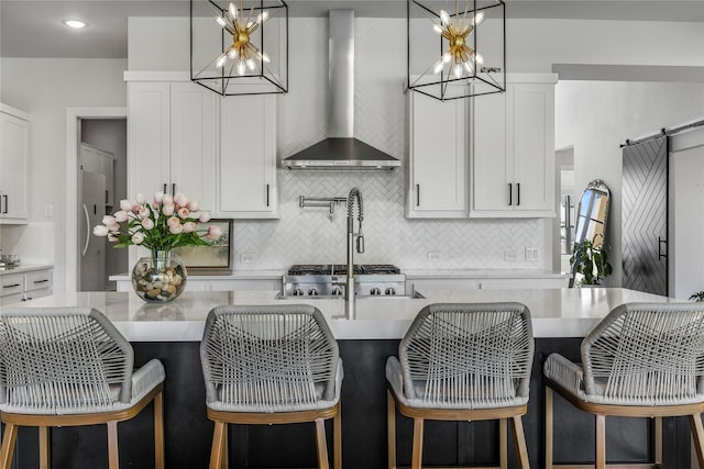 kitchen with a chandelier, a center island with sink, wall chimney range hood, and light countertops