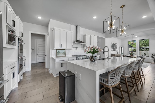 kitchen featuring wall chimney range hood, a chandelier, a sink, decorative backsplash, and a breakfast bar area