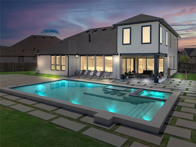 back of house at dusk with a pool with connected hot tub, a patio area, and fence