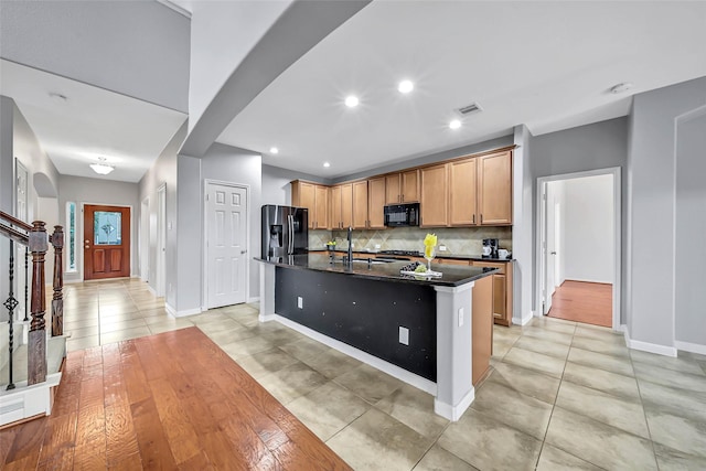 kitchen featuring tasteful backsplash, visible vents, a sink, a kitchen island with sink, and black appliances