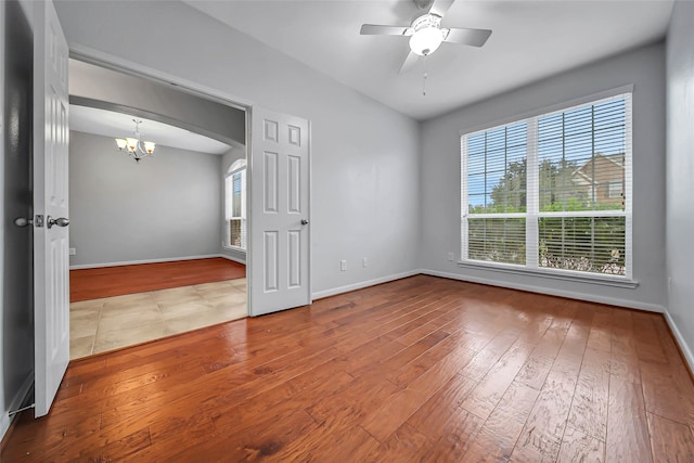 unfurnished room with ceiling fan with notable chandelier, baseboards, and hardwood / wood-style flooring
