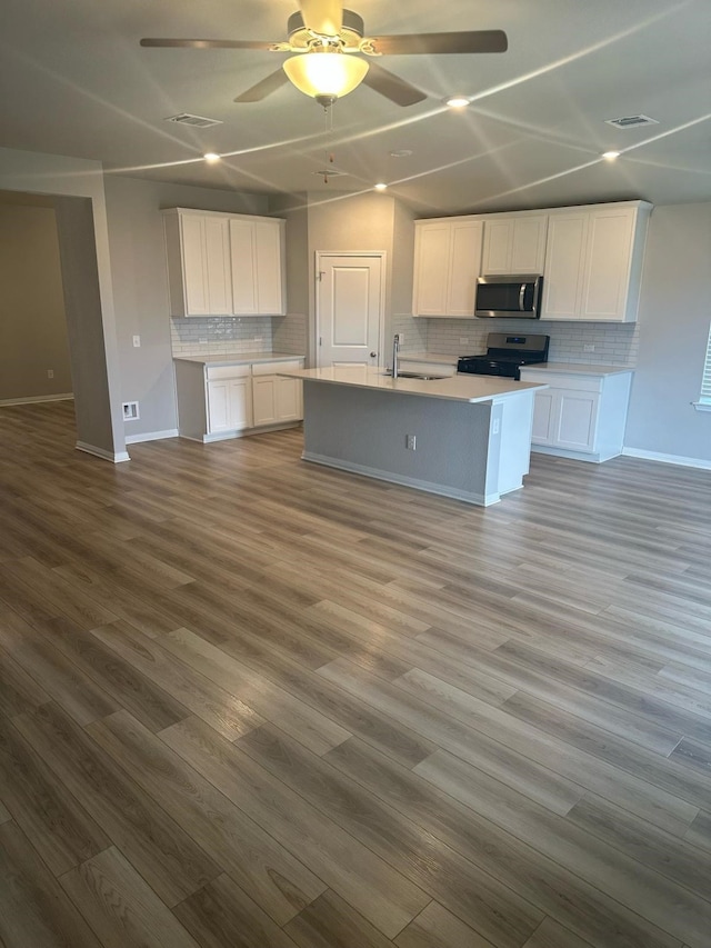 14020 Heartland Dr, Manor, TX 78653 - kitchen with an island with sink, white cabinetry, dark wood-style flooring, light countertops, and stainless steel appliances
