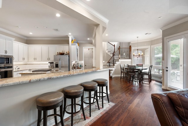 kitchen with white cabinets, appliances with stainless steel finishes, a breakfast bar, a chandelier, and dark wood-style floors