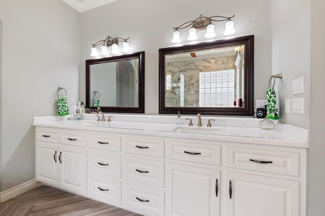 bathroom featuring double vanity, a tile shower, baseboards, and a sink