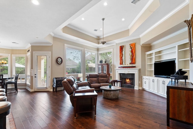 living area featuring dark wood-style floors, a tray ceiling, crown molding, and a warm lit fireplace