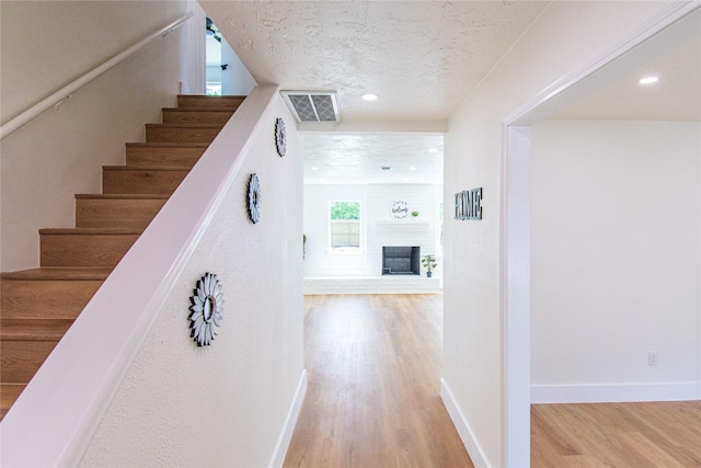 stairway featuring visible vents, baseboards, a brick fireplace, and wood finished floors
