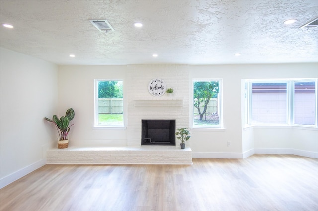 unfurnished living room featuring visible vents, a textured ceiling, plenty of natural light, and wood finished floors
