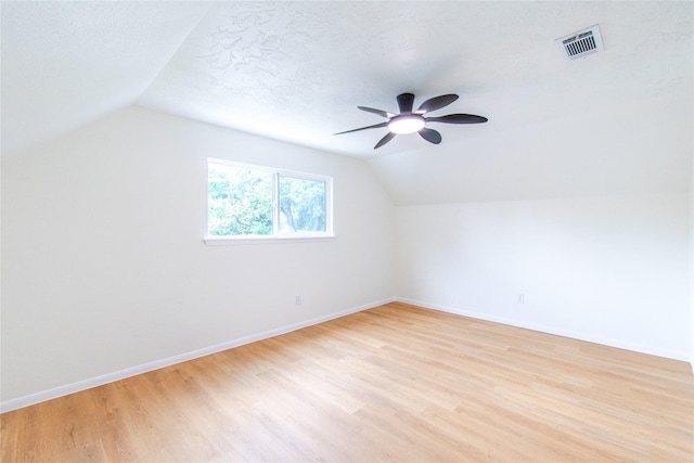 additional living space featuring light wood-style flooring, a ceiling fan, baseboards, vaulted ceiling, and visible vents