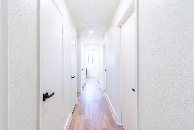 hallway featuring light wood-style floors, a textured wall, and baseboards