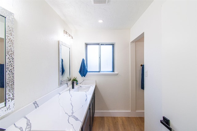 bathroom featuring a textured ceiling, visible vents, wood finished floors, baseboards, and vanity