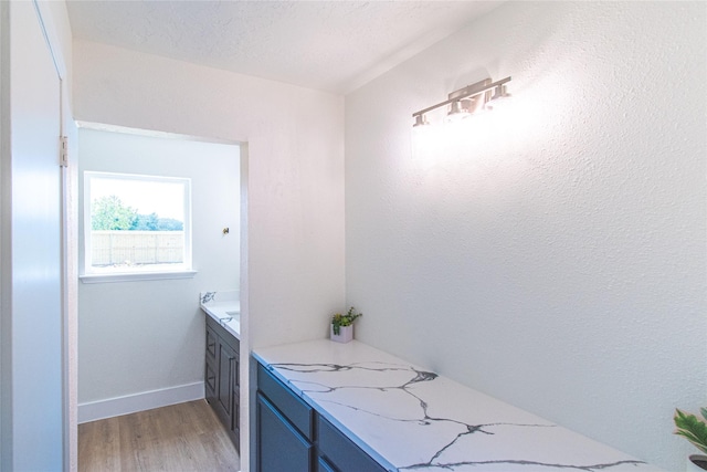 interior space with a textured ceiling, baseboards, wood finished floors, and vanity
