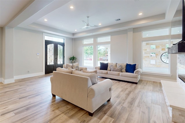 living room featuring a ceiling fan, visible vents, light wood-type flooring, baseboards, and a raised ceiling