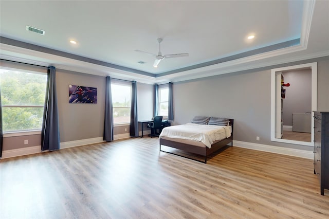 bedroom with baseboards, visible vents, light wood finished floors, and a raised ceiling