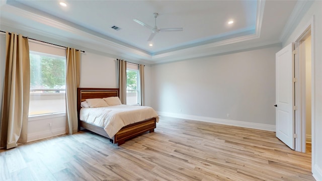 bedroom featuring visible vents, ornamental molding, baseboards, a raised ceiling, and light wood-style flooring