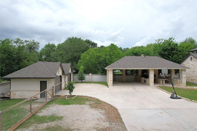 view of front facade with roof with shingles, fence, stone siding, concrete driveway, and an outdoor structure
