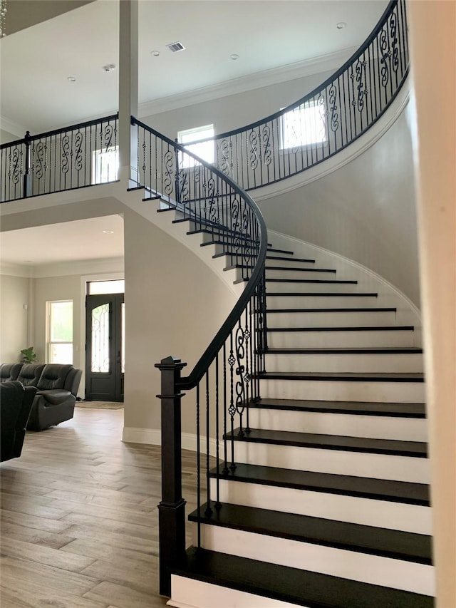 stairs with crown molding, visible vents, a towering ceiling, wood finished floors, and baseboards