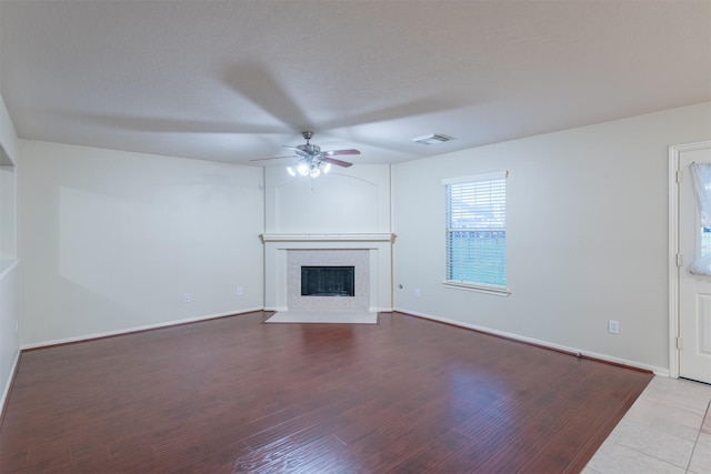 unfurnished living room featuring a ceiling fan, visible vents, wood finished floors, a tile fireplace, and baseboards