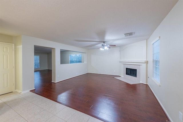 unfurnished living room with a ceiling fan, visible vents, wood finished floors, a tile fireplace, and baseboards