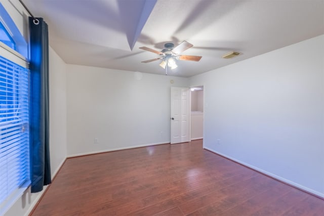 empty room with wood finished floors, ceiling fan, baseboards, and visible vents