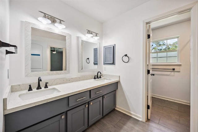 full bath with double vanity, wood finished floors, baseboards, and a sink