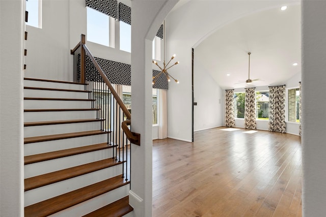 staircase with high vaulted ceiling, arched walkways, a ceiling fan, recessed lighting, and wood finished floors