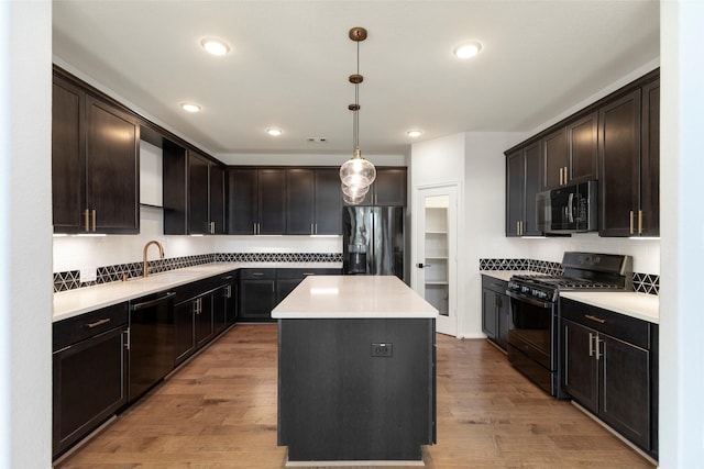 kitchen with light wood-style flooring, light countertops, a kitchen island, black appliances, and a sink