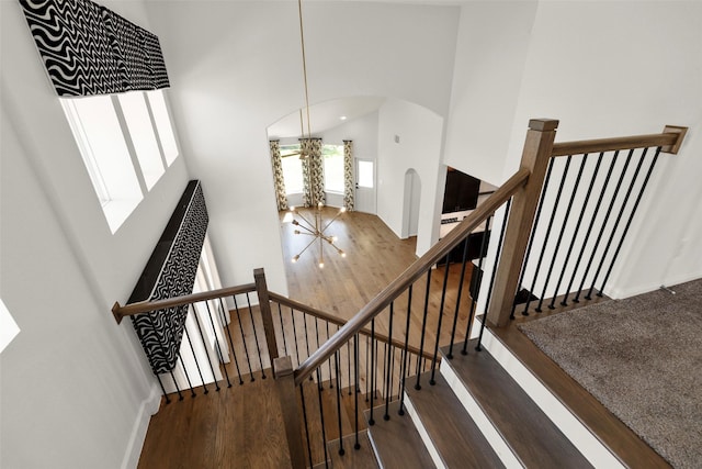 stairway featuring arched walkways, a high ceiling, and wood finished floors