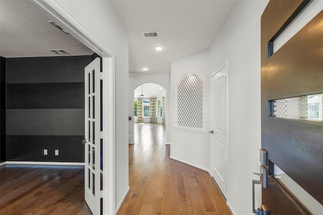 corridor featuring arched walkways, plenty of natural light, visible vents, and wood finished floors