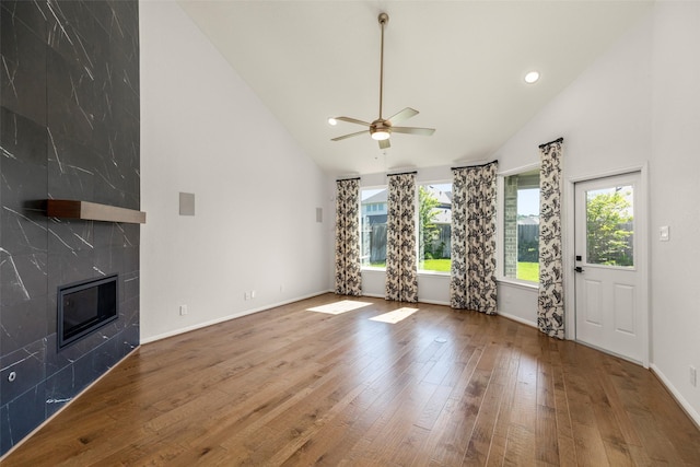 unfurnished living room with high vaulted ceiling, ceiling fan, a fireplace, hardwood / wood-style floors, and baseboards