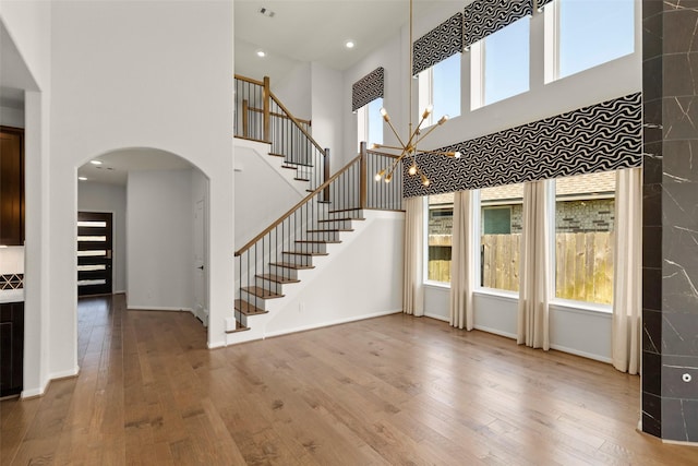 unfurnished living room with wood-type flooring, baseboards, stairway, and arched walkways