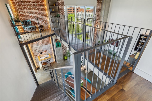 stairway featuring a towering ceiling, wood finished floors, and brick wall