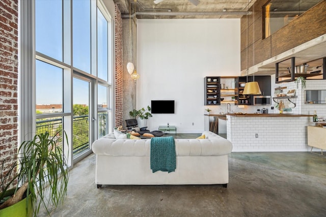 living room featuring concrete flooring, a high ceiling, and brick wall