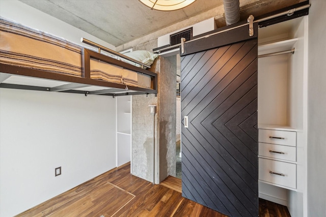 below grade area with wood walls, dark wood-style floors, a barn door, and visible vents
