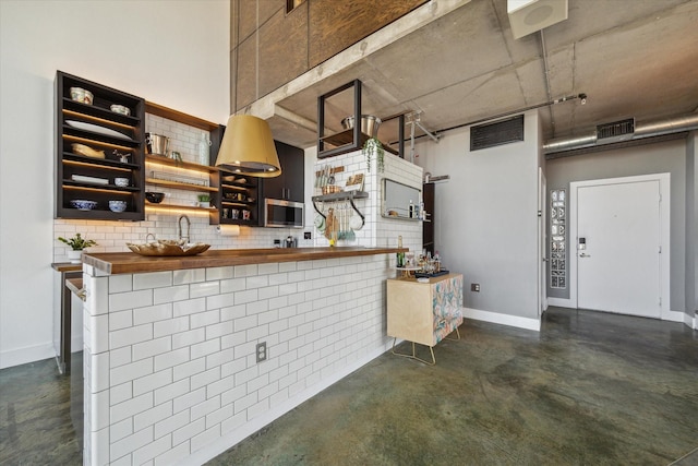 kitchen featuring decorative backsplash, wooden counters, visible vents, stainless steel microwave, and concrete floors