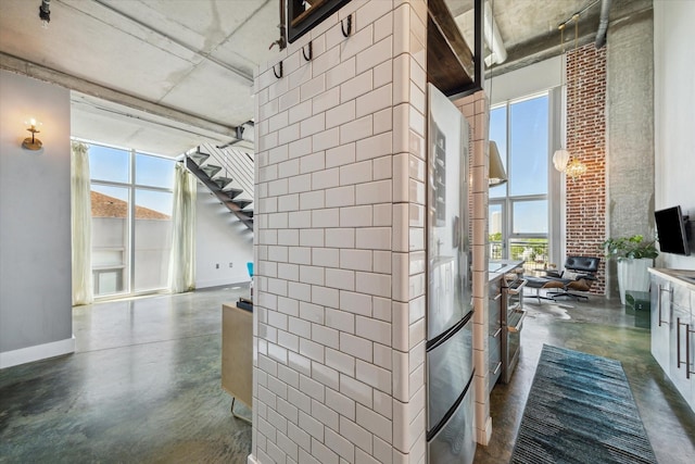 corridor with finished concrete flooring, baseboards, stairway, and a healthy amount of sunlight