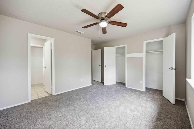 unfurnished bedroom featuring two closets, carpet, connected bathroom, a ceiling fan, and visible vents