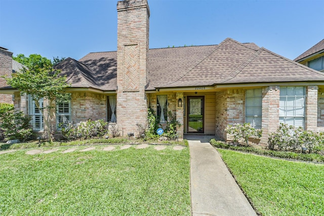 view of front of home with a front lawn, brick siding, a shingled roof, and a chimney