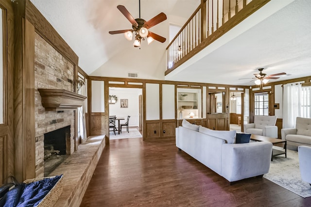 living room featuring a towering ceiling, visible vents, a ceiling fan, a fireplace, and dark wood-type flooring